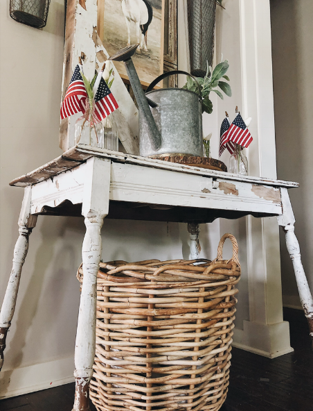 An oversized basket sits underneath a chippy table in our foyer. For further reading on how to create a cozy and inviting entryway, you can head  here.