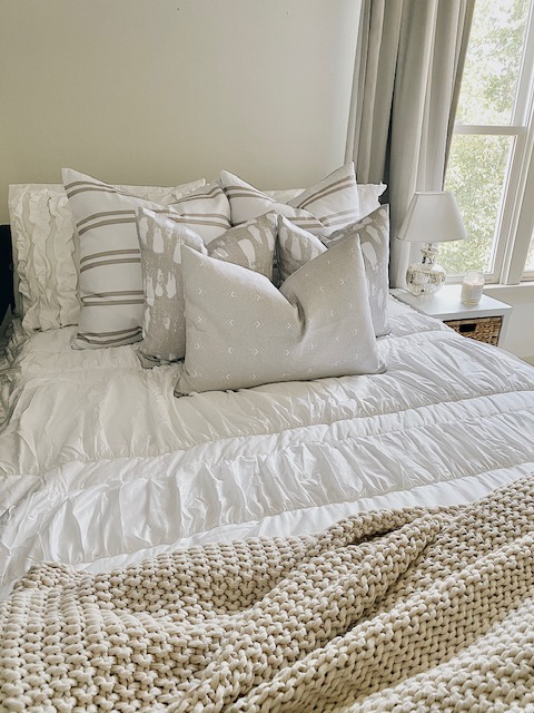 Full view of neutral, farmhouse style pillows on top of white bedding.