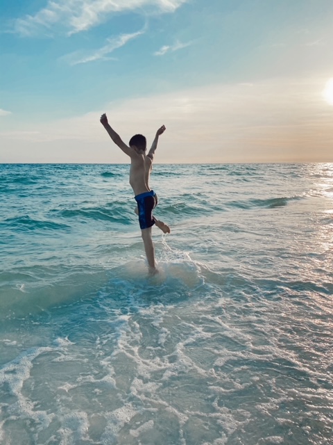 A Complete 30A Travel Guide for Families featured by top US travel blogger, She Gave It A Go | Christian Playlist by popular Alabama lifestyle blog, She Gave It A Go: image of a young boy jumping over small waves in the ocean. 