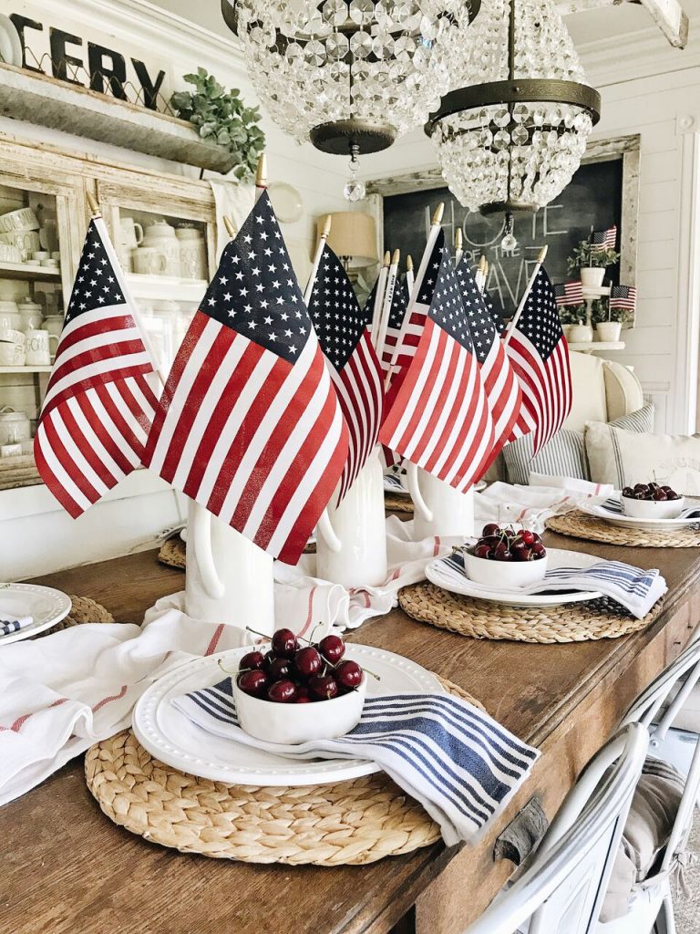 DIY Memorial Day Table Decorations featured by top AL home and lifestyle blogger, She Gave It A Go |Memorial Day Table Top Decorations by popular Alabama DIY blog, She Gave It A Go: image of a wooden table set with sea grass chargers, white plates, white and blue stripe napkins, white bowls filled with cherries, and white pitchers filled with American flags. 