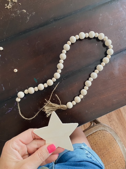 DIY Beaded Garland Tutorial, a summer craft featured by top AL DIY blogger, She Gave It A Go | DIY Beaded Garland by popular Alabama DIY blog, She Gave It A Go: image of a woman holding a wooden star above a beaded garland. 