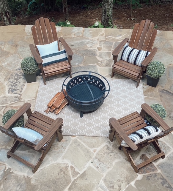 Family Patio Ideas for summer featured by top AL home blogger, She Gave It A Go |  Family Patio Ideas by popular Alabama life and style blog, She Gave It A Go: image of a patio with a black metal fire pit, wooden chairs, potted topiary plants, and a hanging rattan chair.