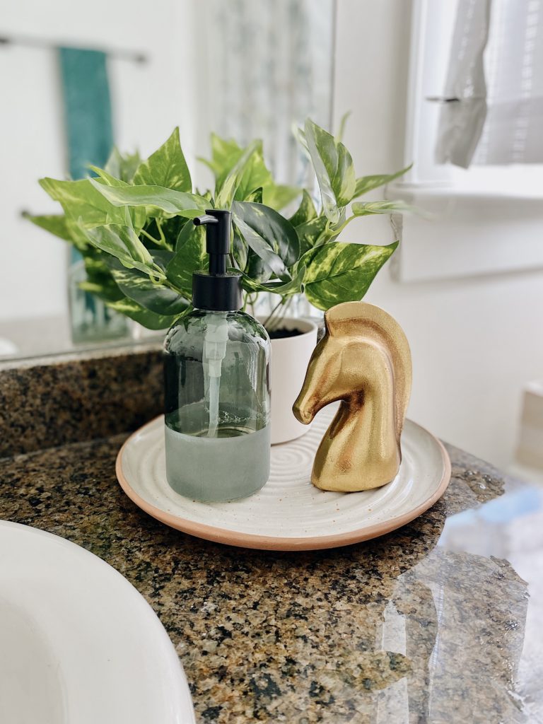 Summer Home Tour 2021: Kitchen, Bathroom, And Teen Girls Room ideas featured by top AL home blogger, She Gave It A Go. | Summer Home Tour by popular Alabama life and style blog, She Gave It A Go: image of a glass soap dispenser bottle, a golden horse head and green potted plant on a round white ceramic dish. 
