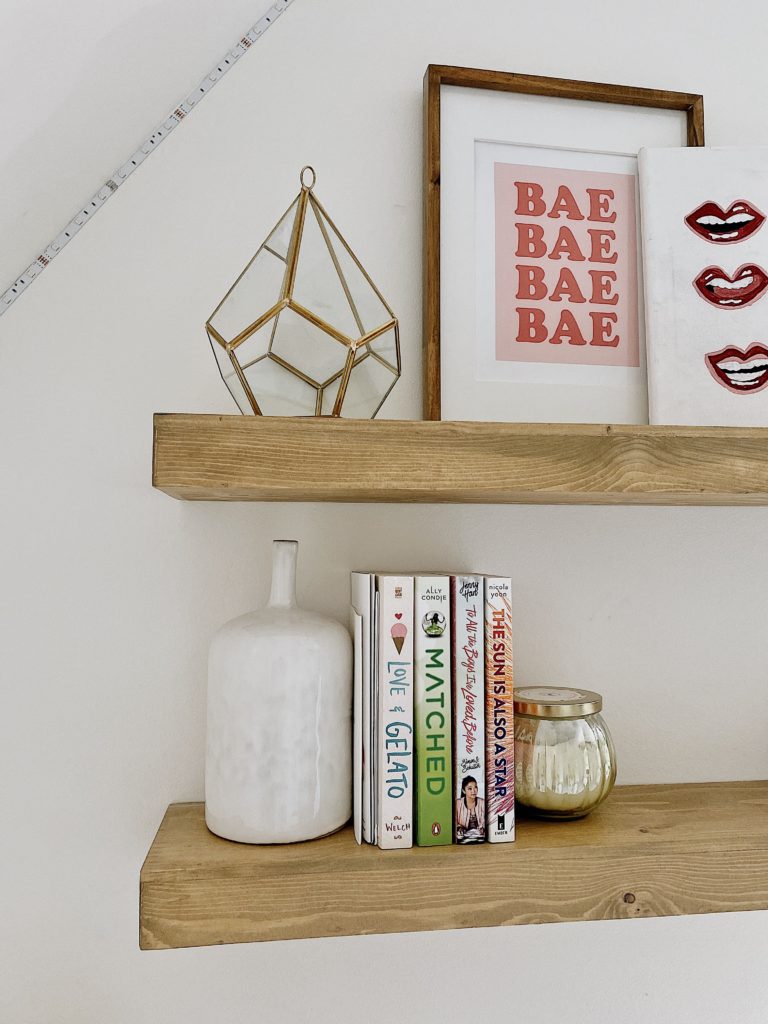 Summer Home Tour 2021: Kitchen, Bathroom, And Teen Girls Room ideas featured by top AL home blogger, She Gave It A Go. | Summer Home Tour by popular Alabama life and style blog, She Gave It A Go: wooden floating shelves decorated with books, a bae art print, gold candle, lip print, and white ceramic vase. 