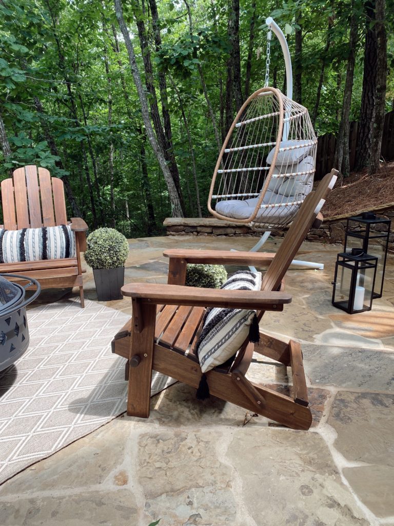 Family Patio Ideas for summer featured by top AL home blogger, She Gave It A Go |  Family Patio Ideas by popular Alabama life and style blog, She Gave It A Go: image of a patio with a black metal fire pit, wooden chairs, potted topiary plants, and a hanging rattan chair.