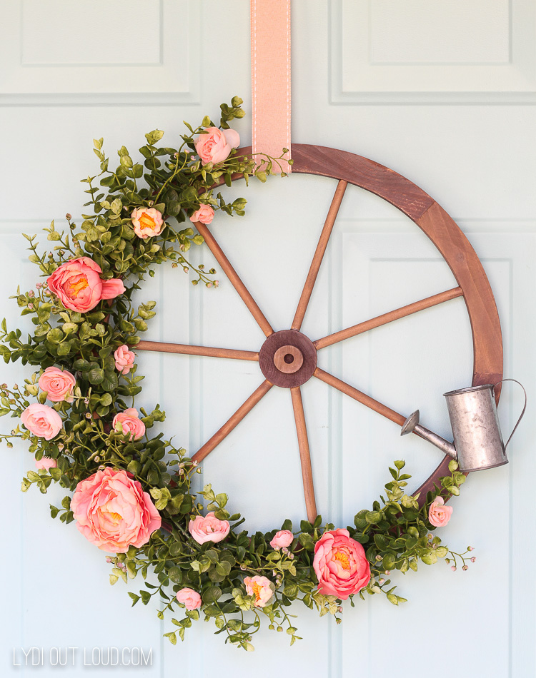 7 Rustic Farmhouse Wreath Ideas for your Summer Front Porch featured by top AL home blogger, She Gave It A Go | Farmhouse Wreath Ideas by popular Alabama life and style blog, She Gave It A Go: image of a wooden wagon wheel wreath with faux pink roses and greenery and a mini tin watering can. 