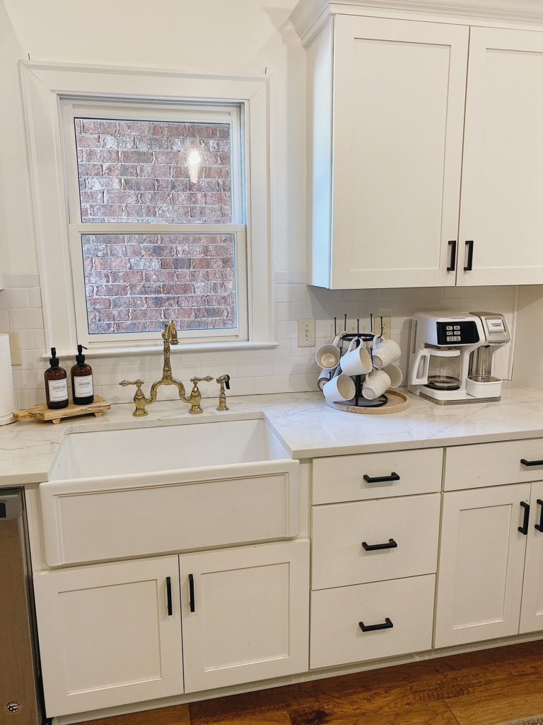 Summer Home Tour 2021: Kitchen, Bathroom, And Teen Girls Room ideas featured by top AL home blogger, She Gave It A Go. | Summer Home Tour by popular Alabama life and style blog, She Gave It A Go: image of a kitchen with a white farmhouse sink, white cabinets, white coffee maker, gold faucet, and lazy Susan filled with white coffee mugs. 