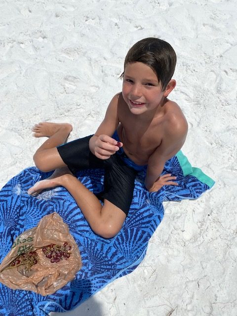 5 Essential Beach Vacation Tips for your Family featured by top AL family blogger, She Gave It a Go | Family Beach Vacation by popular Alabama travel blog, She Gave It A Go: image of a young boy sitting on a blue towel on a white sand beach. 