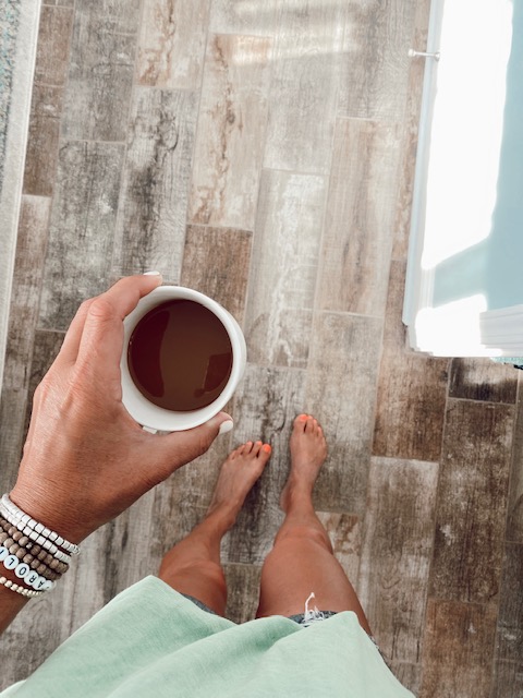 Welcome Home Saturday by popular Alabama lifestyle blog, She Gave It A Go: image of a woman standing on a distressed wood floor and holding white ceramic mug filled with coffee.