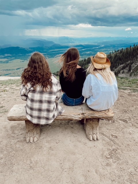 7 Best Things to Do in Jackson Hole with Teens featured by top AL family blogger, She Gave It A Go | Best Things to do in Jackson Hole by popular Alabama travel blog, She Gave it a Go: image of three women sitting on a wooden bench on a mountain top. 