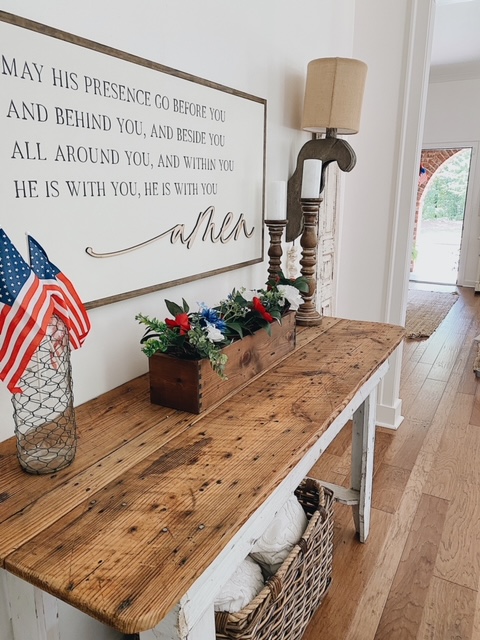 Patriotic Farmhouse Decor featured by top AL home blogger, She Gave It A Go | Patriotic Decor by popular Alabama life and style blog, She Gave It A Go: image of a white farmhouse entry table decorated with a faux red, white, and blue floral arrangement and mini American flags in a glass vase covered in chicken wire. 