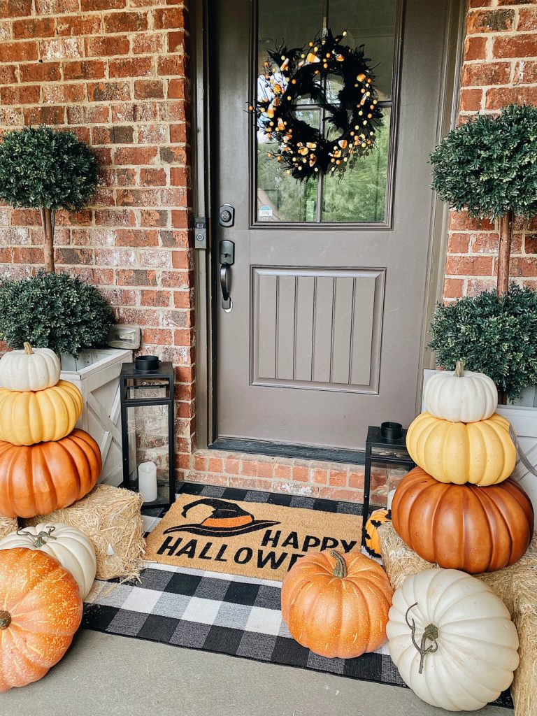 front door with Halloween wreath, pumpkins, and fall outdoor mats