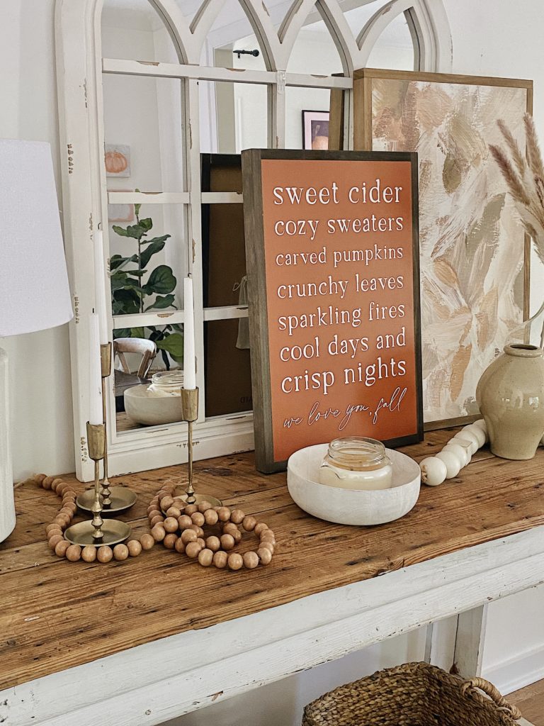 console table with wood beads, layered signs, candles, and mirror