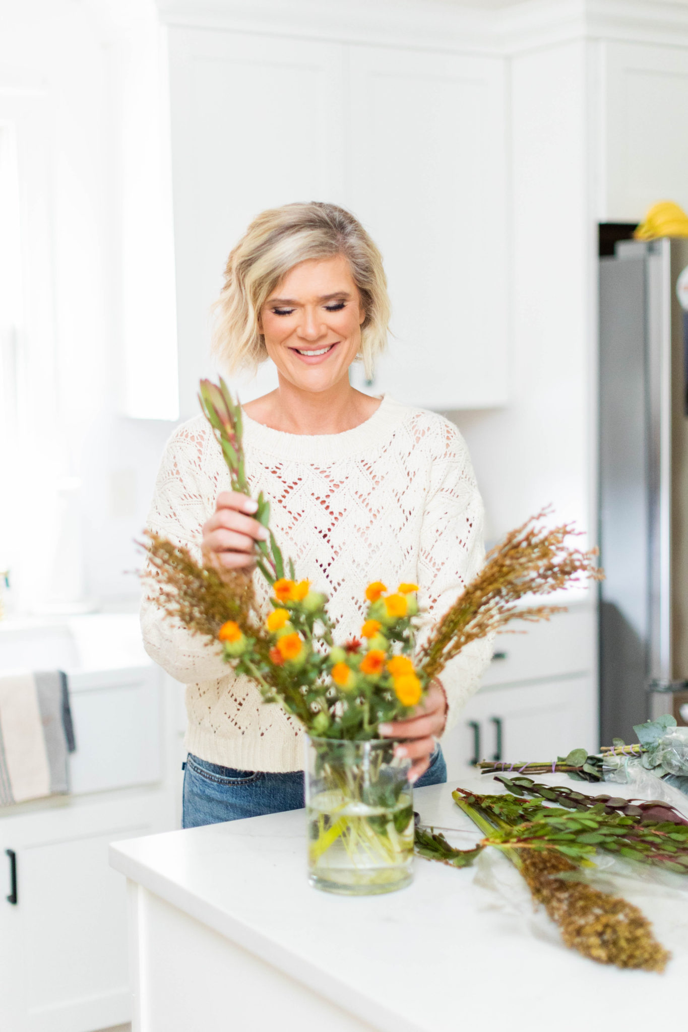 woman standing by kitchen island styling fall stems in a vase