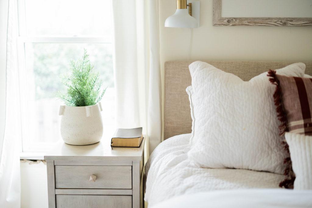 bed with white quilt and pillow and a nightstand with a plant