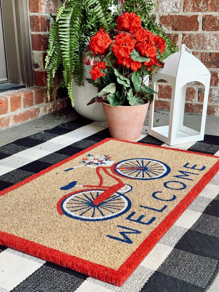 doormat with bicycle on it, red geraniums, white lantern