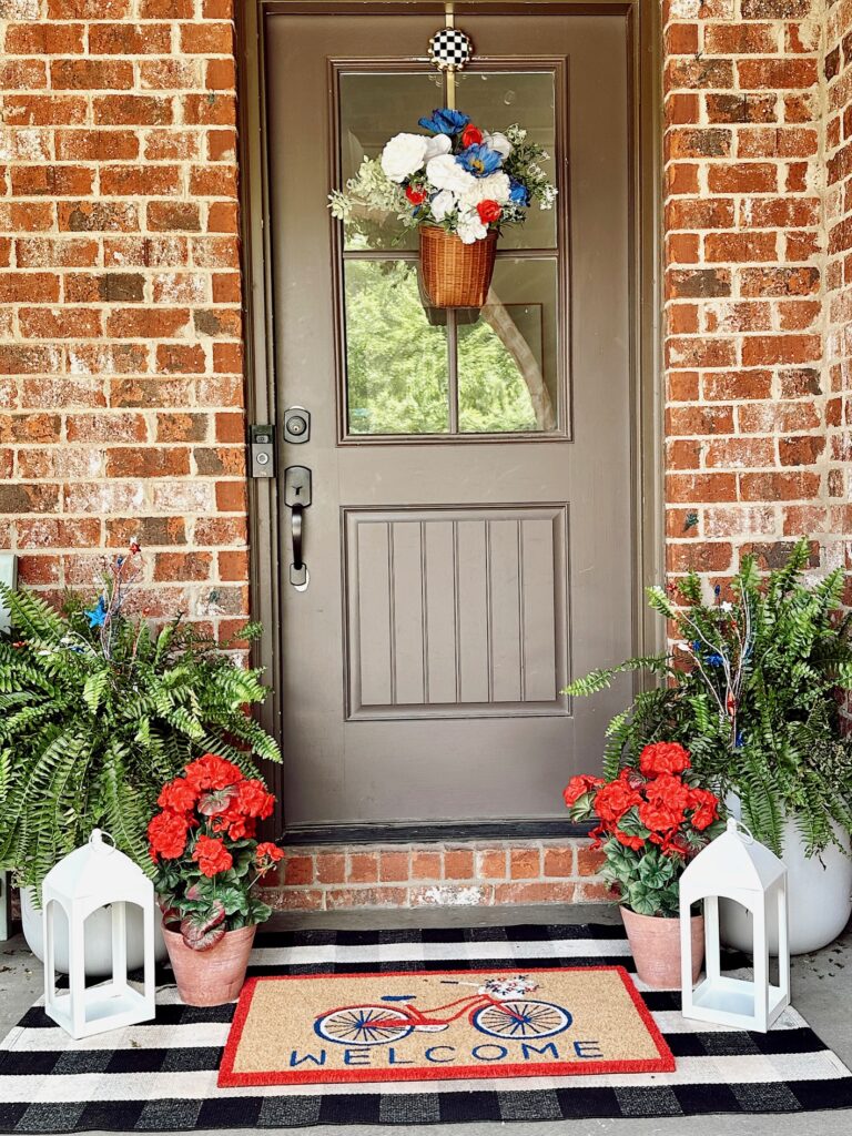 Front door with hanging basket, geraniums, lanterns, and ferns