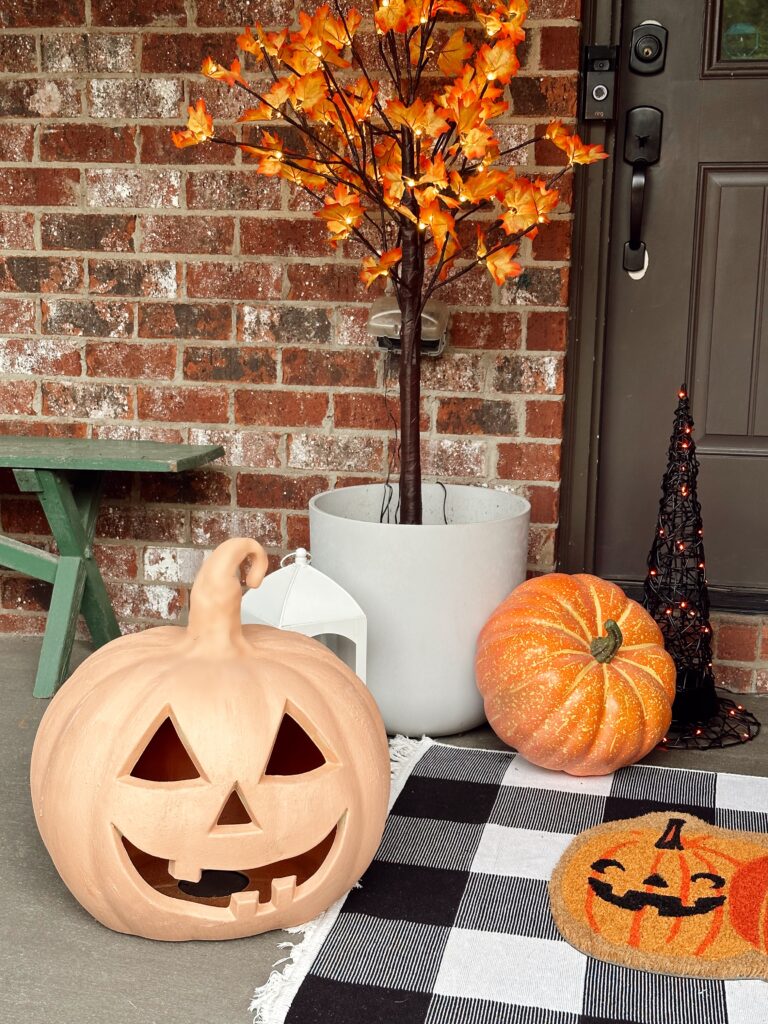 DIY Terracotta pumpkin on porch with black and white check rug and maple trees