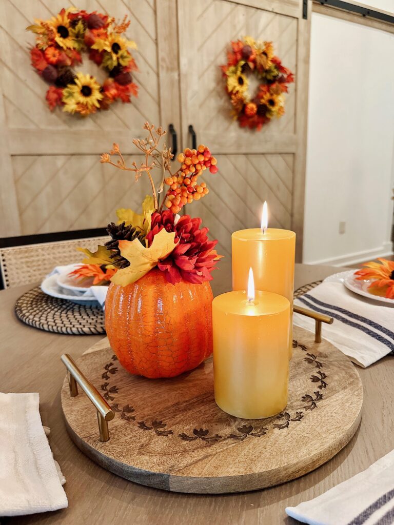 rustic wood tray with pumpkin and two lit candles for table centerpiece